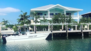 A white house with a balcony, a dock with a boat named "COOLE CAT", and palm trees in the background. - Grouper House: 4 Masters/6 BA, Pool/Dock, BoatRamp (Marathon)