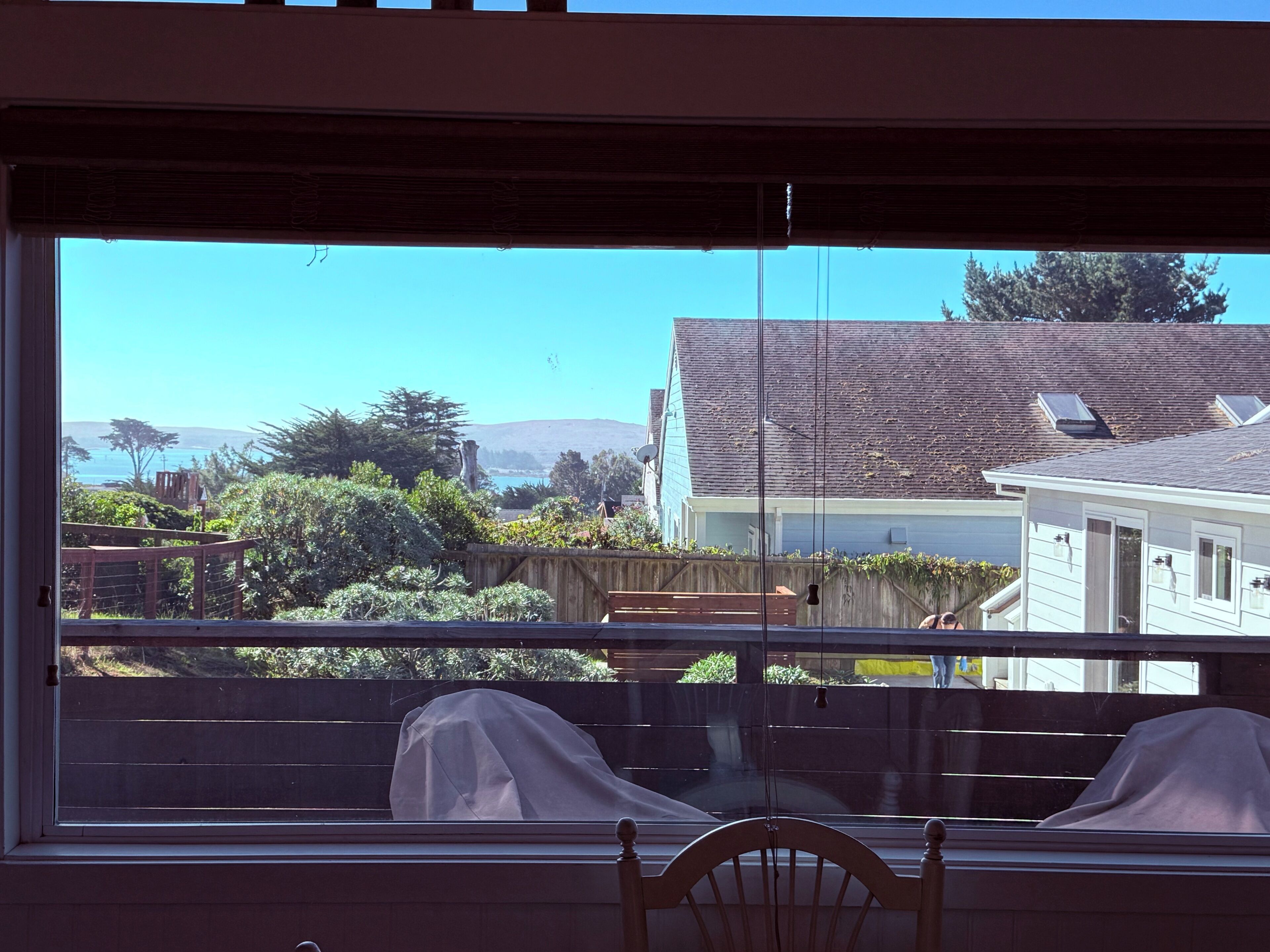 Une vue par la fenêtre, avec une chaise en bois et une table recouverte d’un tissu.