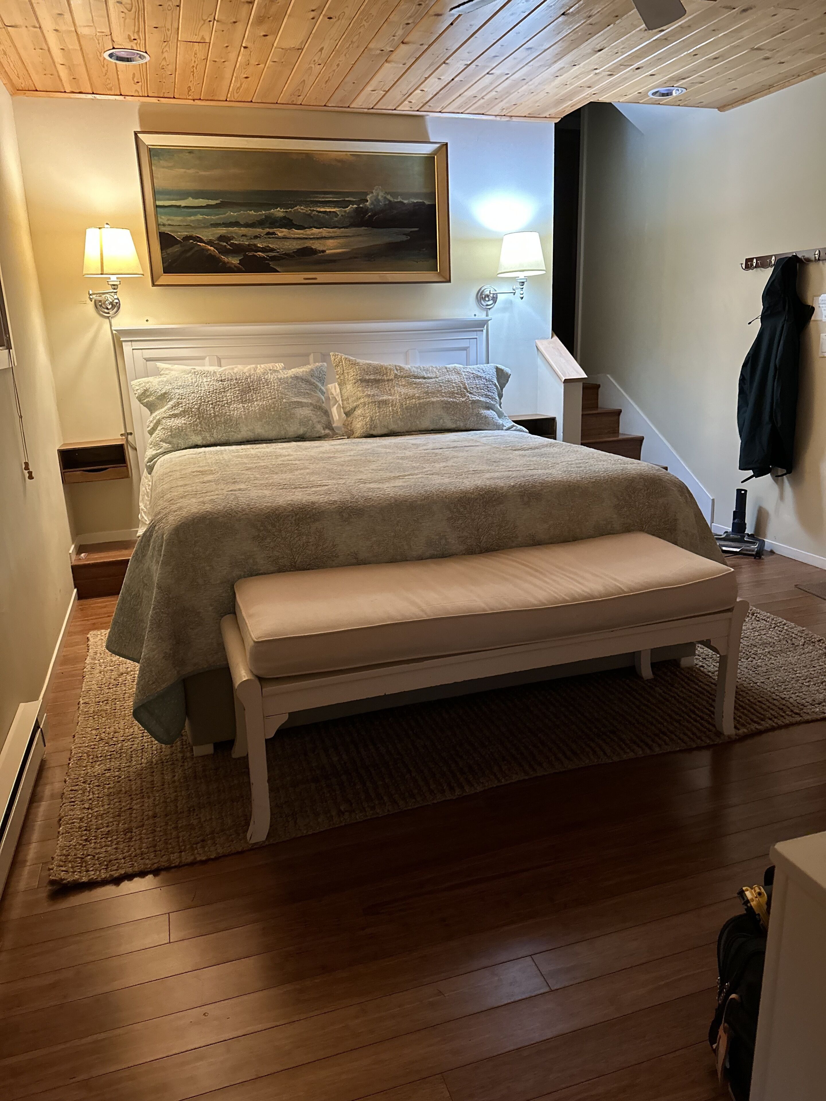 Une chambre à coucher avec un lit, des lampes de chevet, un tableau et un escalier.