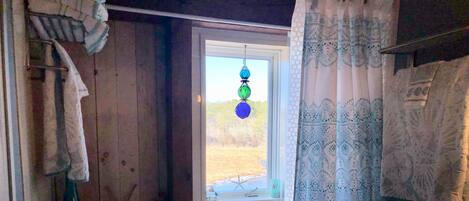A bathroom with a bathtub, a window with a view of a grassy field, and a curtain with a geometric pattern.