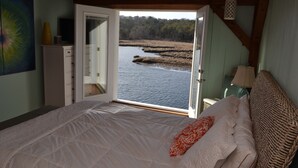 A bedroom with a large bed, a view of a river, and a door leading outside. - The Perfect Waterfront Home, mins from downtown and beaches! Getaway this summer (East Falmouth)