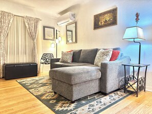 A living room with a grey sofa, patterned cushions, a patterned rug, a black side table with a lamp, and a framed picture on the wall. - Perfect family friendly home in Nob Hill (Albuquerque)