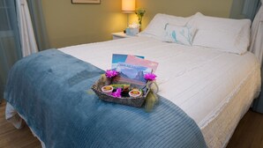 A neatly made bed with a blue blanket, a bedside table with a lamp, and a small basket with travel brochures and a flower. - Perfect family friendly home in Nob Hill (Albuquerque)