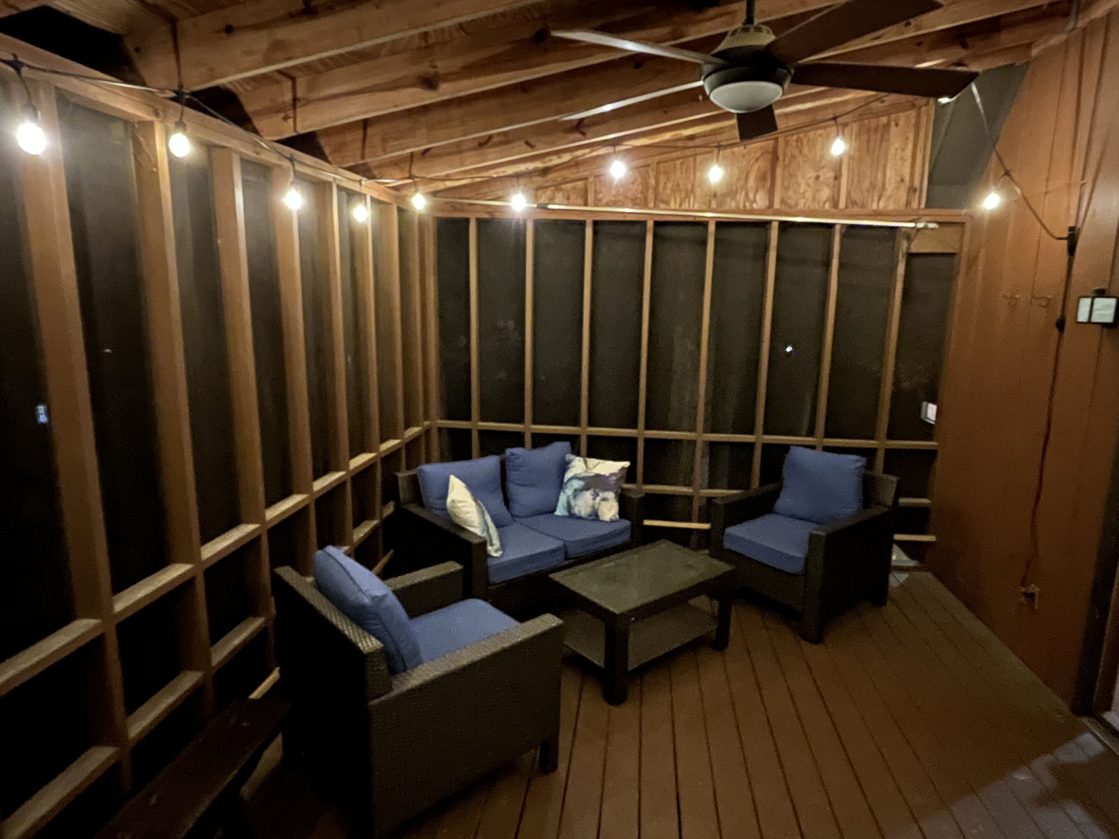 A wooden deck with a sofa and chairs, a ceiling fan, and string lights.