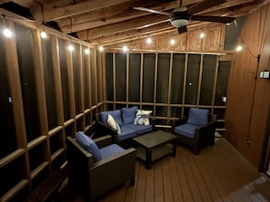 Une terrasse en bois avec un canapé et des fauteuils, un ventilateur de plafond et des guirlandes lumineuses.
