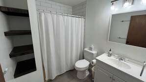 Ein Badezimmer mit Toilette, Duschvorhang, Waschbecken mit Spiegel und integrierten Regalen.