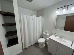Un baño con inodoro, cortina de ducha, lavamanos con espejo y estantes empotrados.