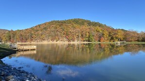 Ein ruhiger See mit einem hölzernen Steg und einem bewaldeten Hügel im Hintergrund.