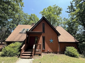 Une cabane en bois avec une porte rouge, un emblème en forme d’étoile et un petit porche.