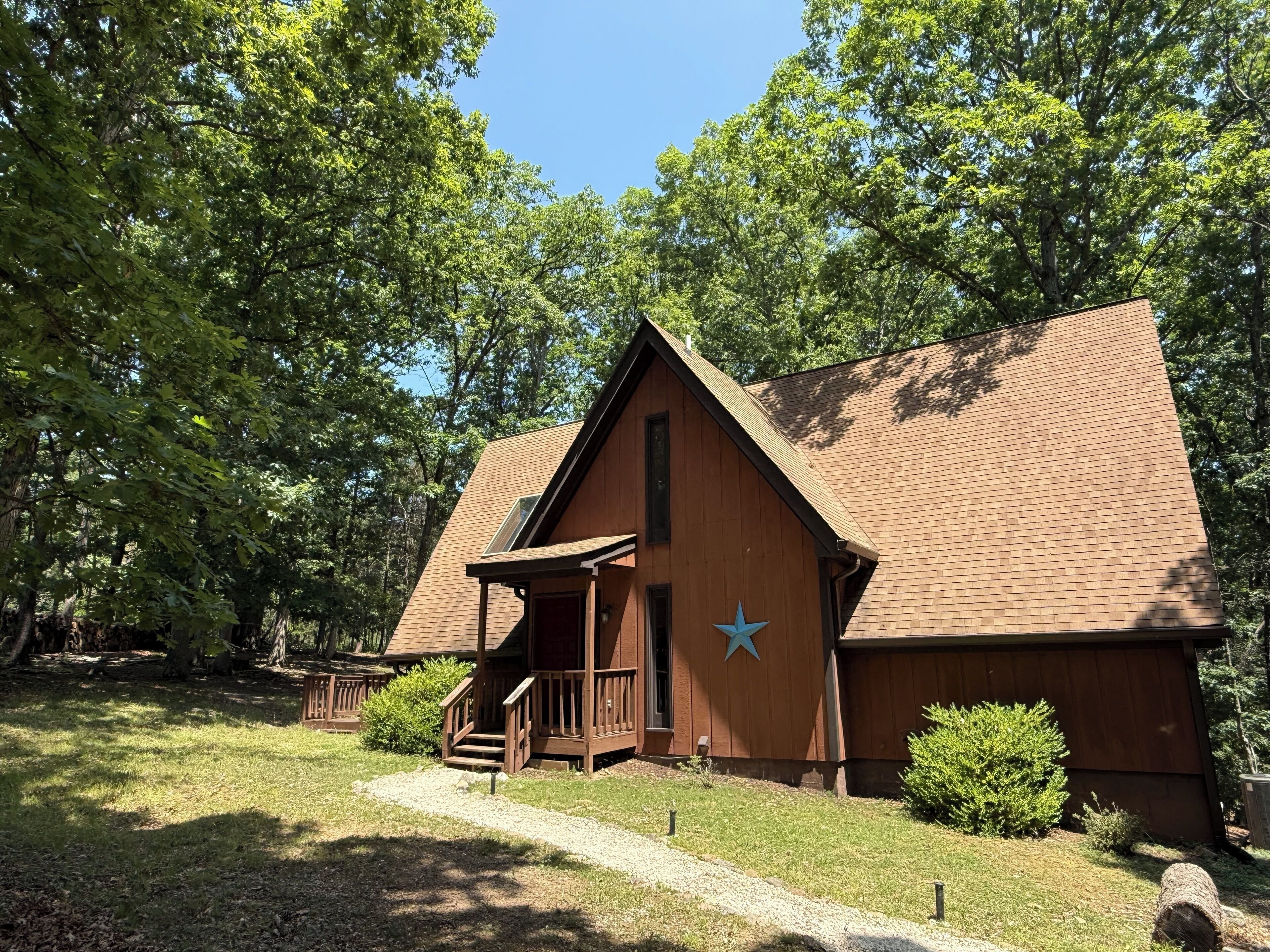 A wooden cabin with a star emblem, surrounded by trees and a gravel path.