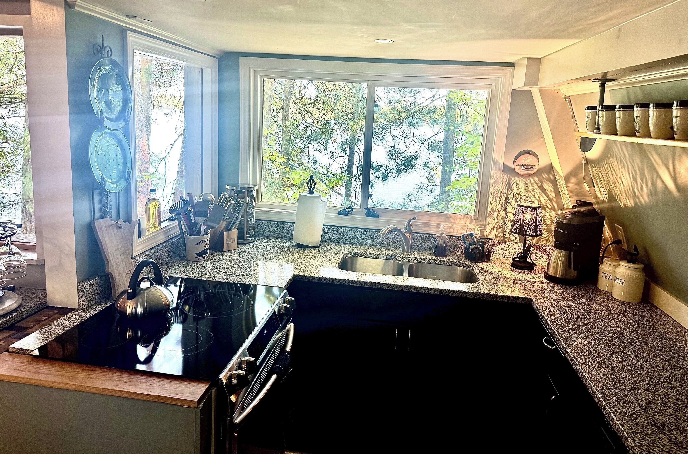 A kitchen with a black stovetop, a sink, and a window with a view of trees.