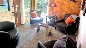 Een knus vertrek met houten wanden, een open haard, een eettafel en uitzicht op groen.