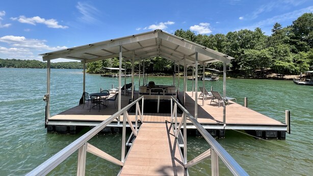 A covered dock with seating and a table, surrounded by water and trees.