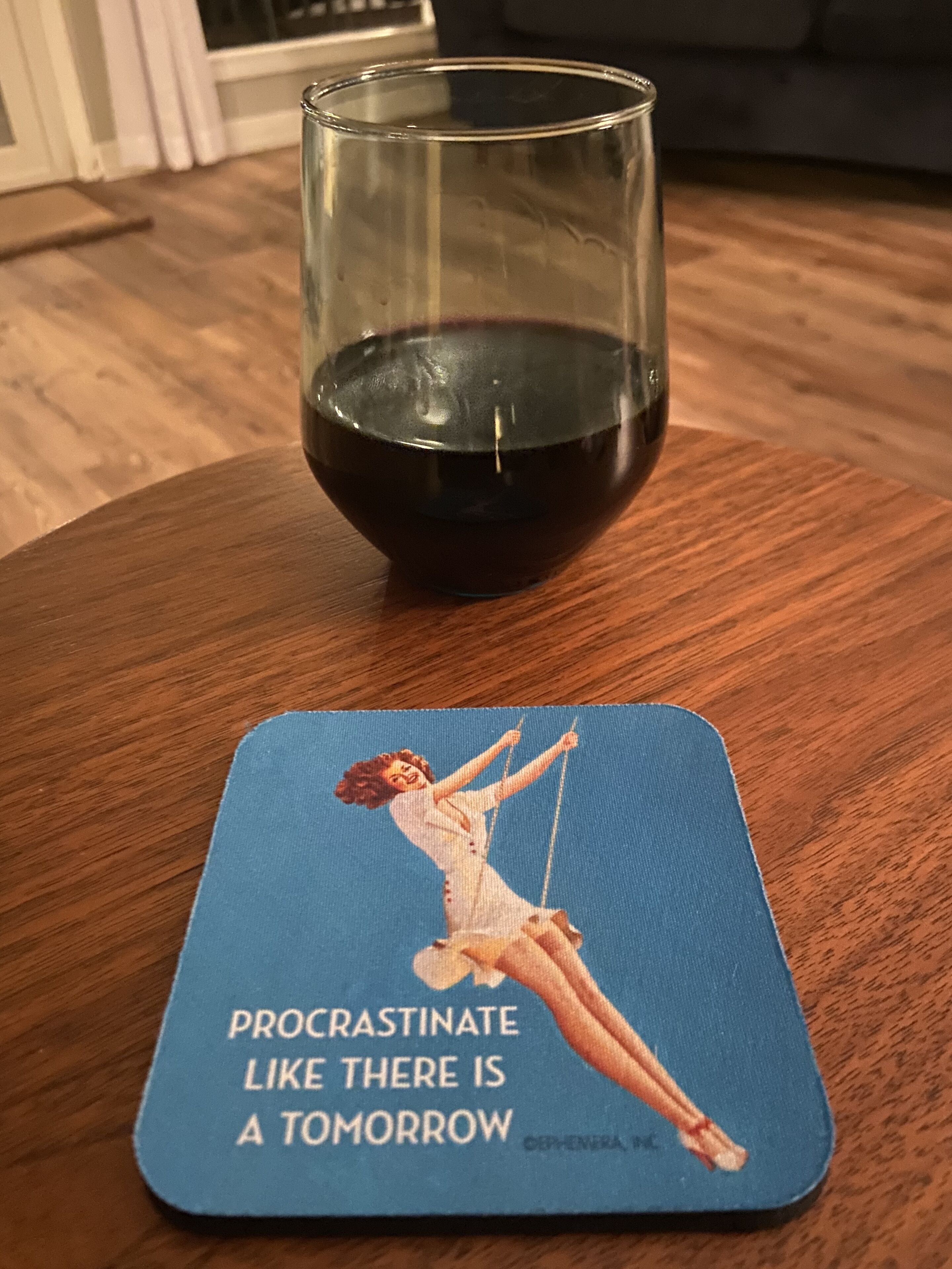 A glass of red wine on a wooden table with a coaster featuring a quote.