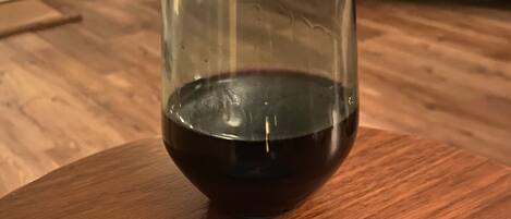 A glass of red wine on a wooden table with a coaster featuring a quote.
