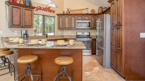 A kitchen with wooden cabinets, a central island with stools, a refrigerator, and a coffee maker.