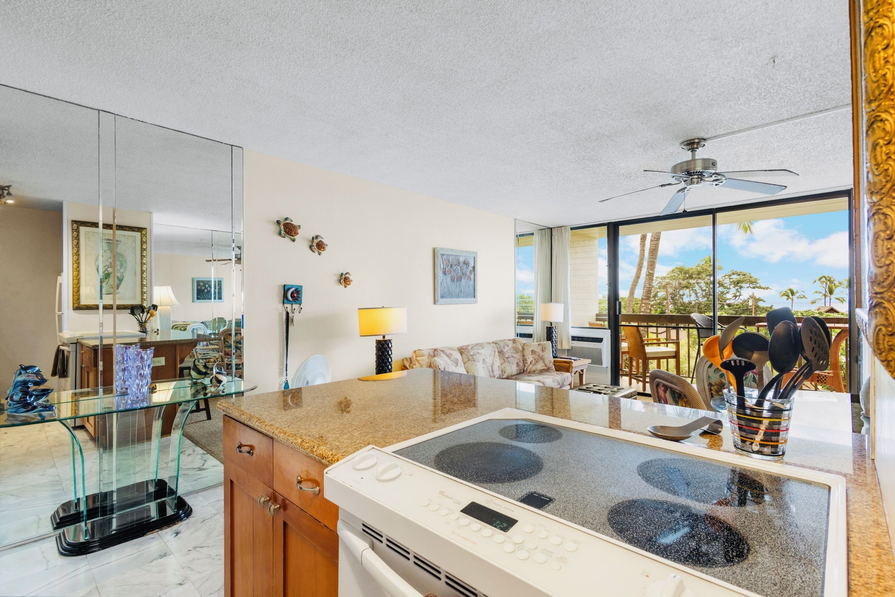 Una cocina moderna con estufa integrada, mesa de vidrio para comer y grandes ventanales con vista a palmeras.