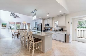 Una cocina moderna con una isla central, muebles blancos y una zona de comedor con sillas de madera.