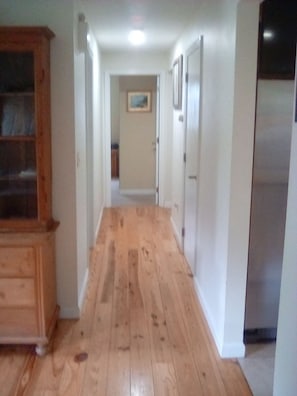 Un pasillo con piso de madera, paredes blancas y un refrigerador a la derecha.