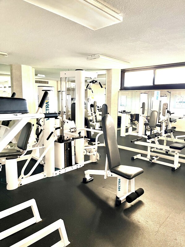A gym with various exercise machines, including a bench press and a leg press. - Luxury Oceanfront Condo with Reduced Rates! (Myrtle Beach)