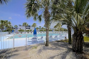 A pool area with a fenced deck, palm trees, and a building in the background.