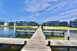 A wooden pier leading to a row of modern buildings with a clear sky above.