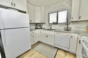 A kitchen with white cabinets, a stainless steel sink, and a window with blinds.