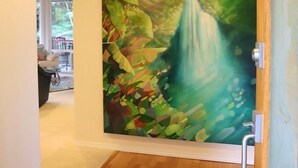 A hallway with a wooden floor and a large mural of a waterfall and foliage on the wall. - Gorgeous! The Waterfall Retreat At Reed's Island (Hilo)