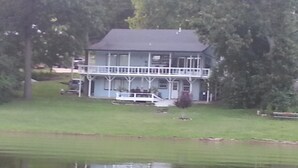 Een woonhuis met twee verdiepingen, een veranda en een klein steigertje dat in het water uitsteekt.