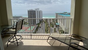 A balcony with a view of a beach, buildings, and a tennis court.