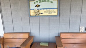A wooden bench seating area with a sign above reading "Our Beach House" and a small table in the center.