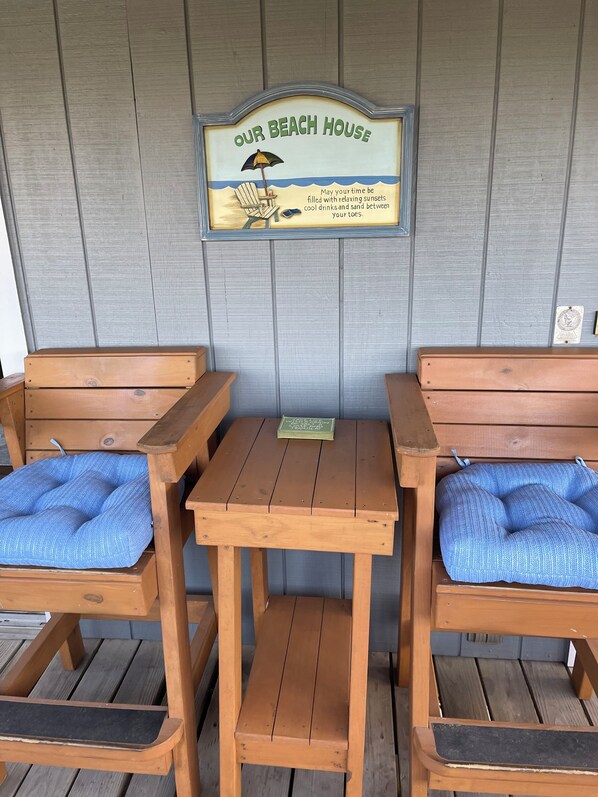 Zona de asientos con banco de madera, un letrero arriba que dice "Our Beach House" y una pequeña mesa en el centro.