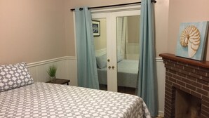 A bedroom with a checkered bedspread, a small bedside plant, a fireplace, and a door with blue curtains.