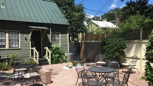A patio area with outdoor furniture, a green building, and a wooden fence.