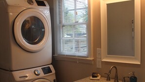 A laundry area with stacked washers and dryers, a sink with a mirror, and a window with blinds.