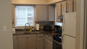A compact kitchen with wooden flooring, a built-in oven, a microwave, and a refrigerator.