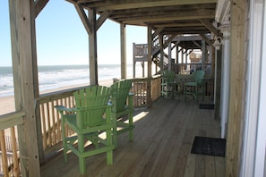A wooden deck with green chairs overlooking the beach.