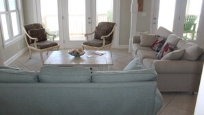 Ein Wohnzimmer mit einem hellblauen Sofa, zwei Sesseln, einem Couchtisch und einem beigefarbenen Sofa mit bunten Kissen.