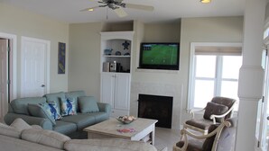 Ein Wohnzimmer mit einer Couch, Sesseln, einem Couchtisch, einem Kamin und einem Fernseher.