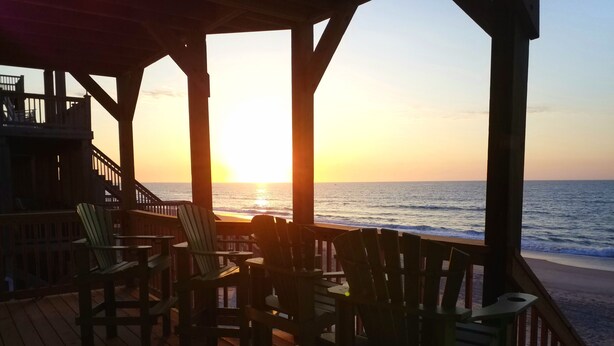 Eine Holzterrasse mit Stühlen, die auf den Sonnenuntergang über dem Meer blickt.