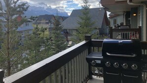 Ein Balkon mit Grill, der auf einen Wohnbereich mit Häusern und Bergen im Hintergrund blickt.
