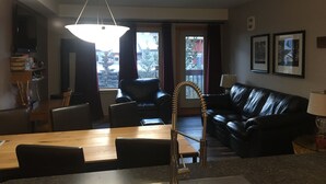 Ein modernes Wohnzimmer mit Essbereich, einer schwarzen Ledersofa, einem Holzessttisch und einer Chandelier.