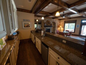 A kitchen with granite countertops, wooden cabinets, a stone fireplace, and a dining area with chairs. - Gorgeous lakefront home with infinity pool, pickleball court, stunning lake view (Dawsonville)