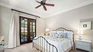 Un dormitorio con cama, mesita de noche, lámpara, ventilador de techo y vistas a través de un ventanal.