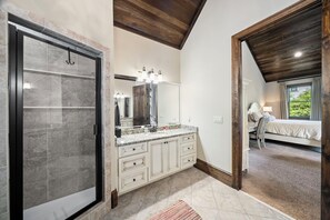 A modern bathroom with a large mirror, a shower enclosure, and a vanity with a granite countertop. - Gorgeous lakefront home with infinity pool, pickleball court, stunning lake view (Dawsonville)