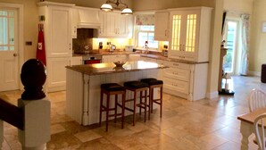 A spacious kitchen with a large island, white cabinetry, and a chandelier. - Luxurious Cottage Set in Beautiful Irish Countryside. (Nenagh)