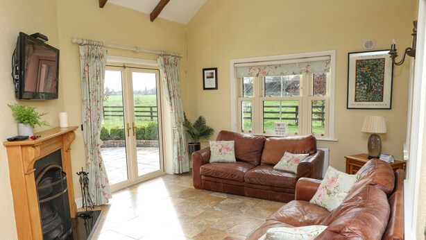 A cozy living room with a fireplace, leather sofas, and a large window with a view of the garden. - Luxurious Cottage Set in Beautiful Irish Countryside. (Nenagh)
