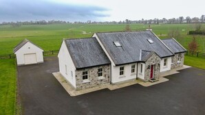 A two-story stone house with a red door, a small attached garage, and a paved driveway. - Luxurious Cottage Set in Beautiful Irish Countryside. (Nenagh)