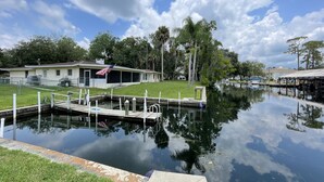 A calm water body with a dock, a house with an American flag, and surrounding greenery. - Waterfront in Crystal River! Scalloper's Heaven, Boaters Dream, see manatees (Crystal River)