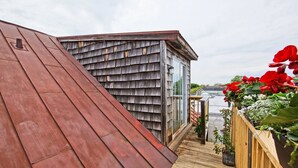 A wooden deck with a metal roof, a glass door, and a wooden fence with plants. - The Rodney House (Lewes)